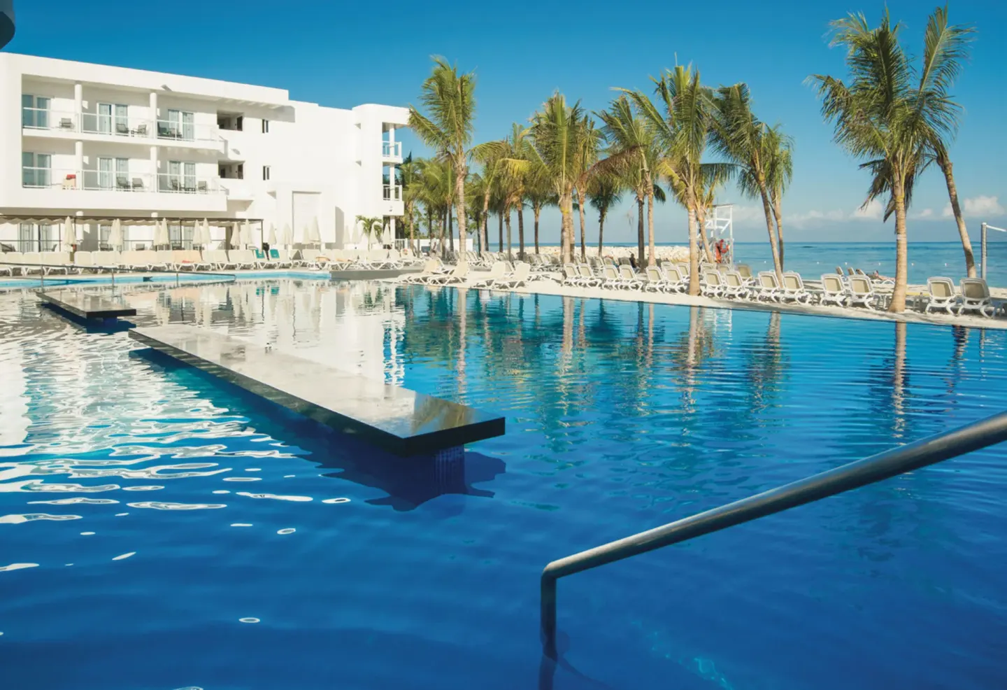 Quiet pool with palm trees, loungers, and ocean beyond at Hotel Riu Reggae.