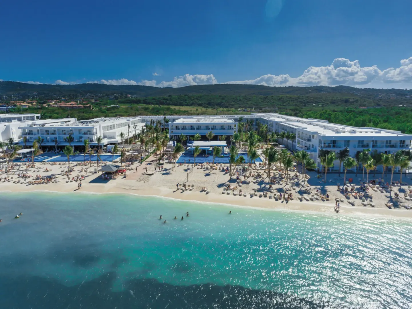 Wide aerial view of Hotel Riu Reggae, showing white resort buildings, beach, and clear sea.