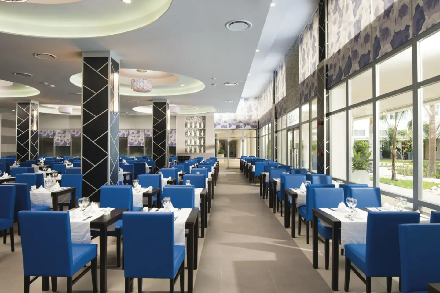 Large dining room with blue chairs and floor-to-ceiling windows at Hotel Riu Reggae.