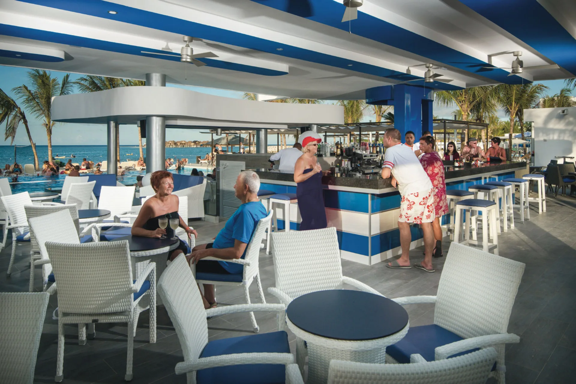 Poolside bar seating and guests by the sea at Hotel Riu Reggae.