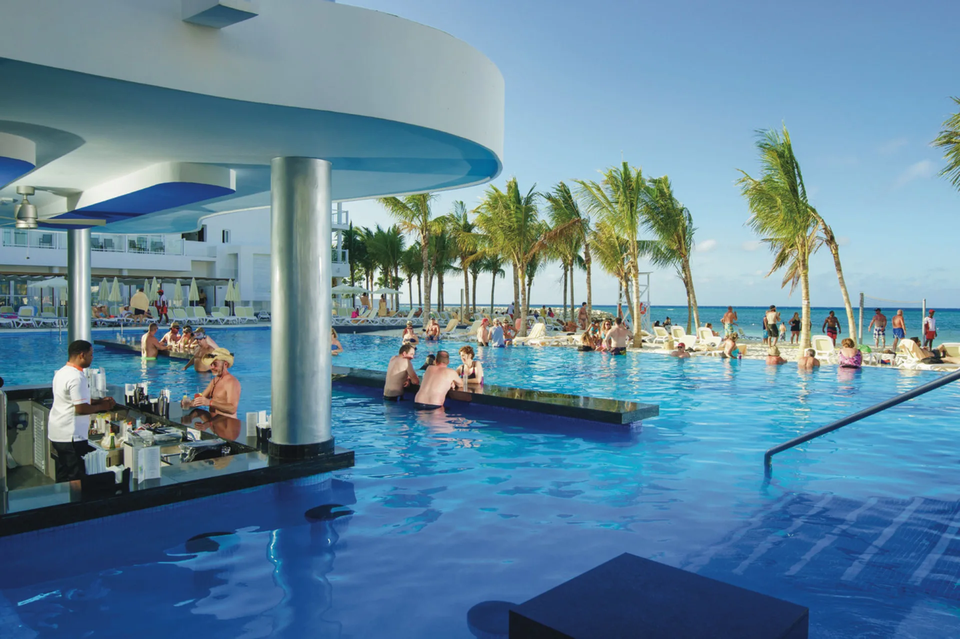 Swim-up pool bar with guests and ocean views at Hotel Riu Reggae.