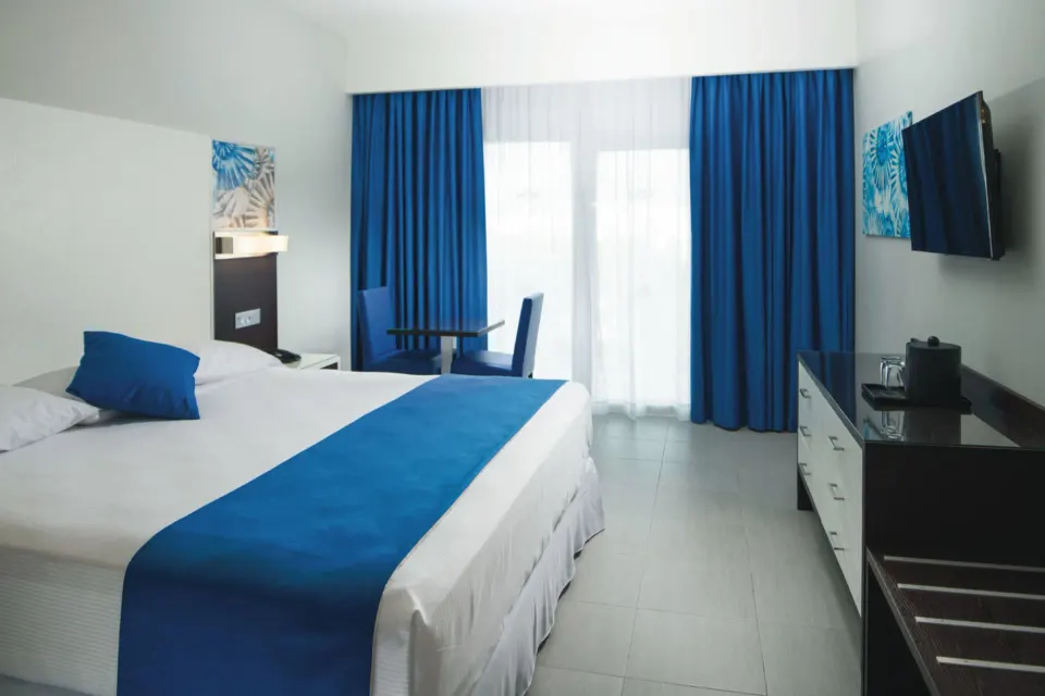 Tropical view room with one bed, blue curtains, TV and seating area at Hotel Riu Reggae.