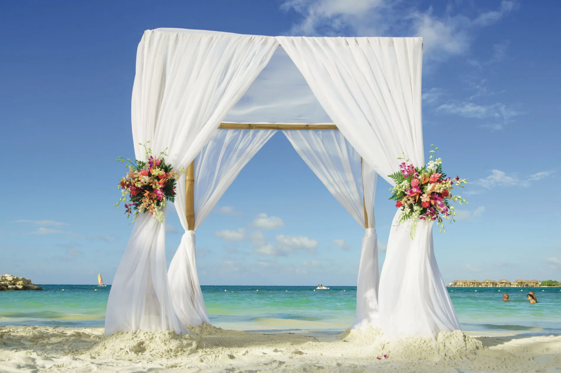White beach wedding arch with flowers by the sea at Hotel Riu Reggae.