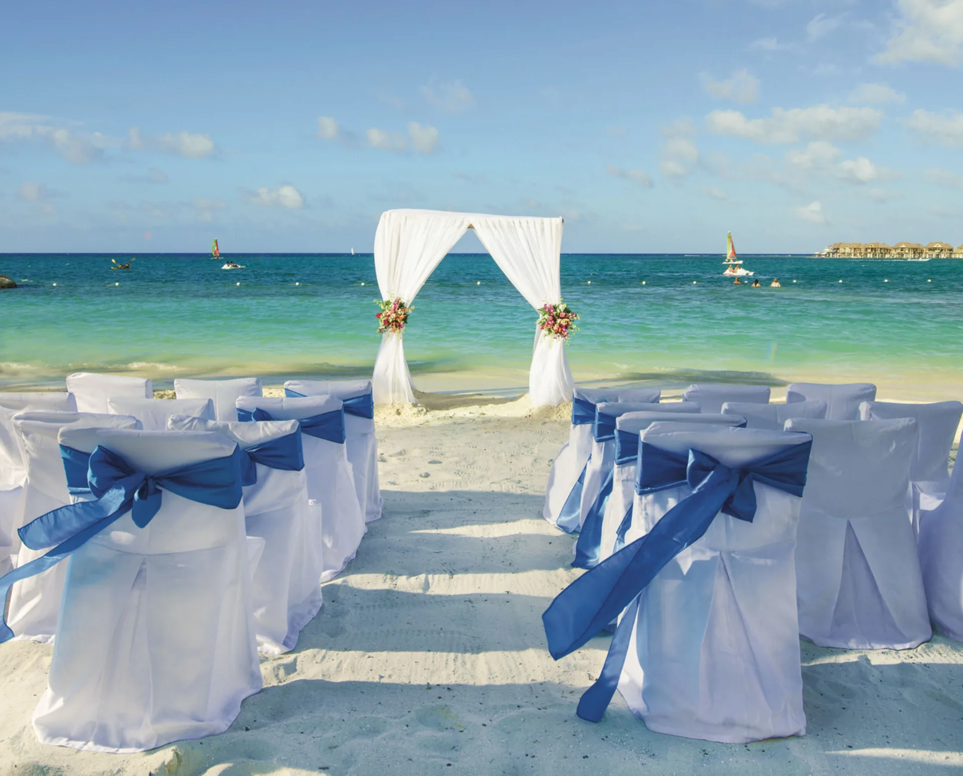 Beach wedding setup with white chairs and blue sashes at Hotel Riu Reggae.