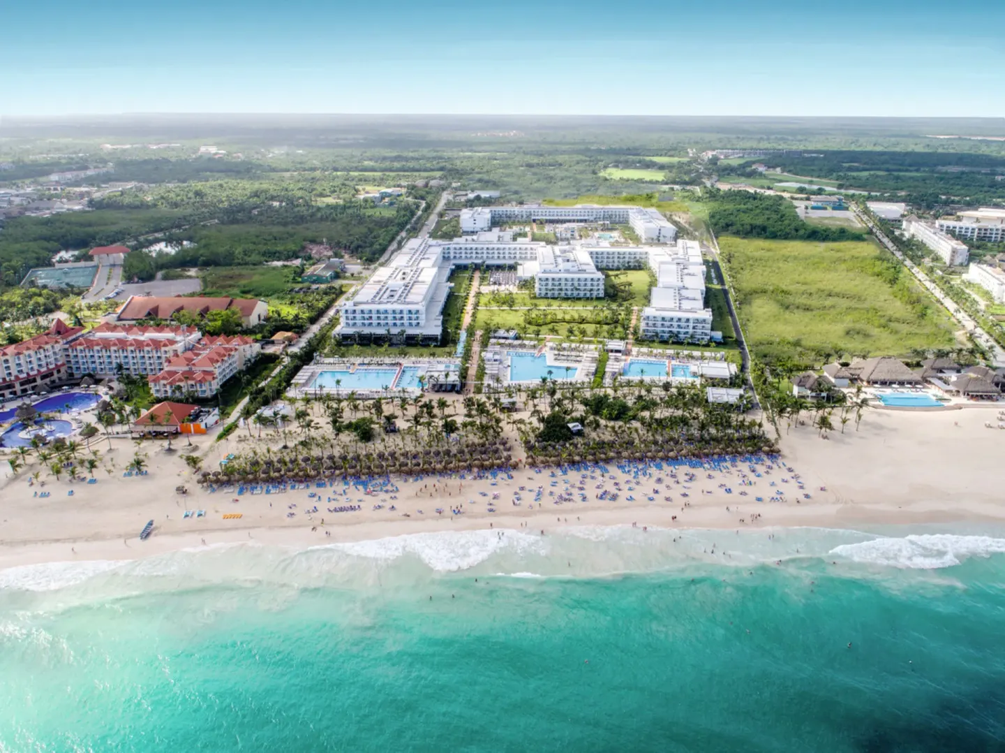Aerial view of Hotel Riu Republica beside the beach with pools, buildings, and turquoise water.