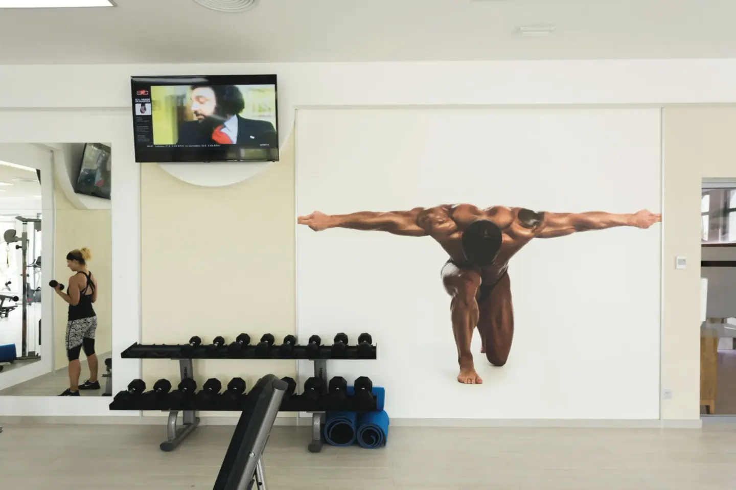 Dumbbell racks, exercise mats, mirror, and wall graphic in the gym at Hotel Riu Republica.