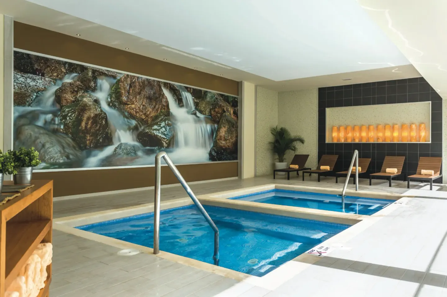 Indoor spa pool with loungers and waterfall wall art at Hotel Riu Republica.