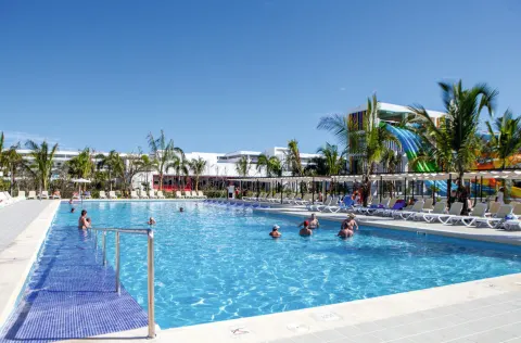 Long pool with guests, loungers and waterslides in the background at Hotel Riu Republica.