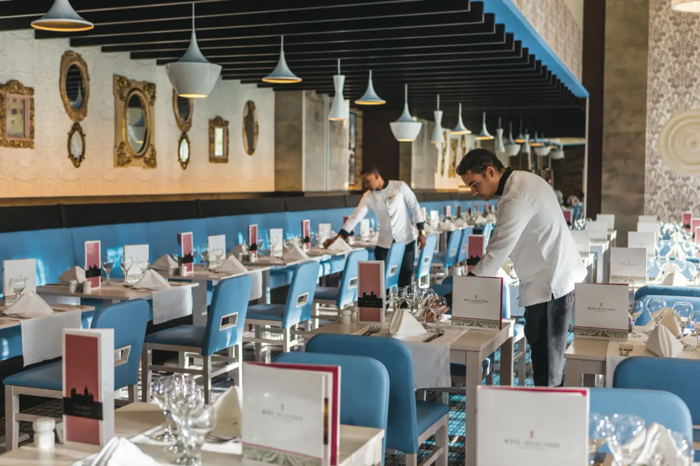 Staff set tables in an Italian-style dining room with blue chairs at Hotel Riu Republica.