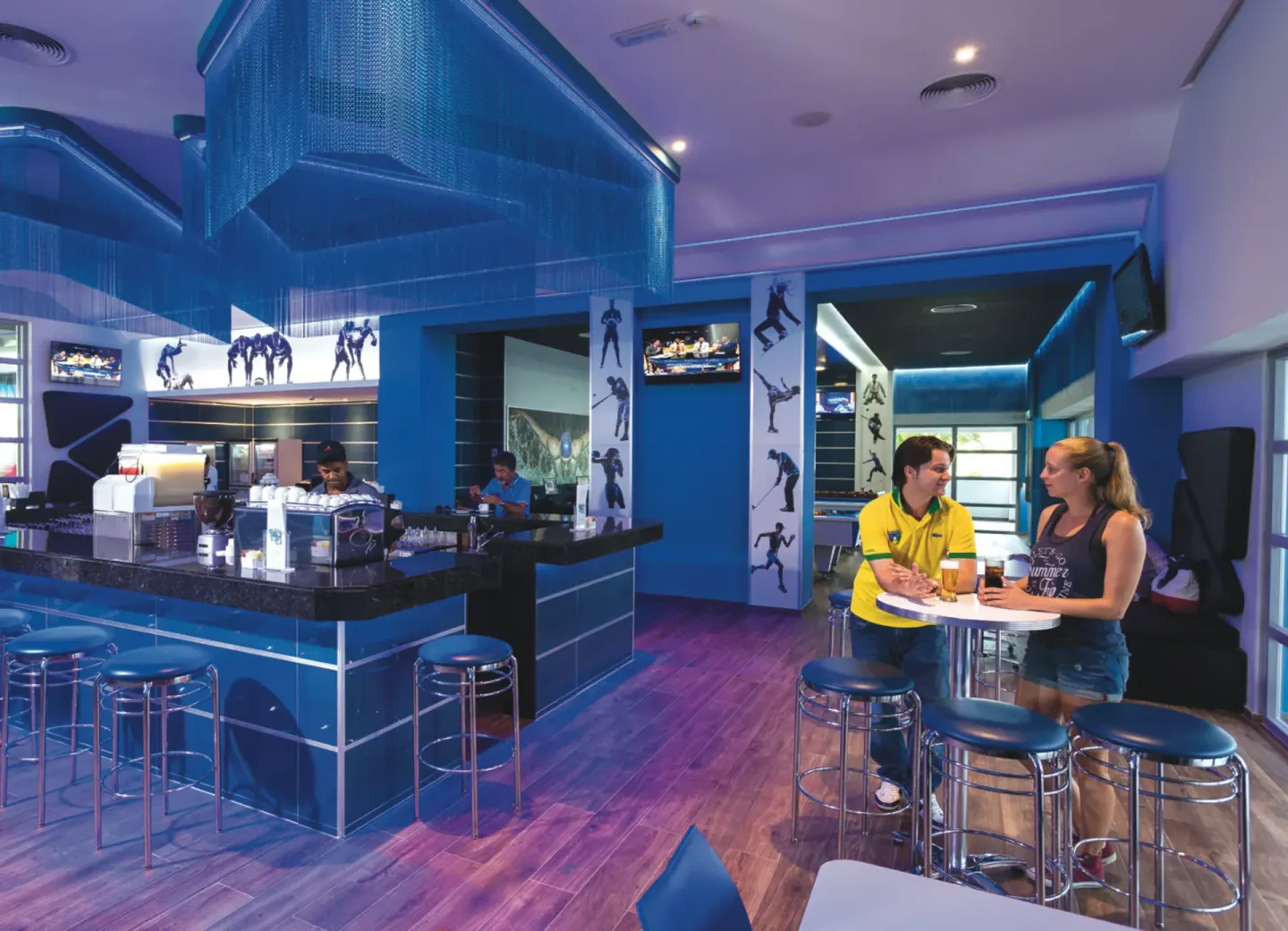 Blue sports bar with stools, TVs, and guests at Hotel Riu Republica.