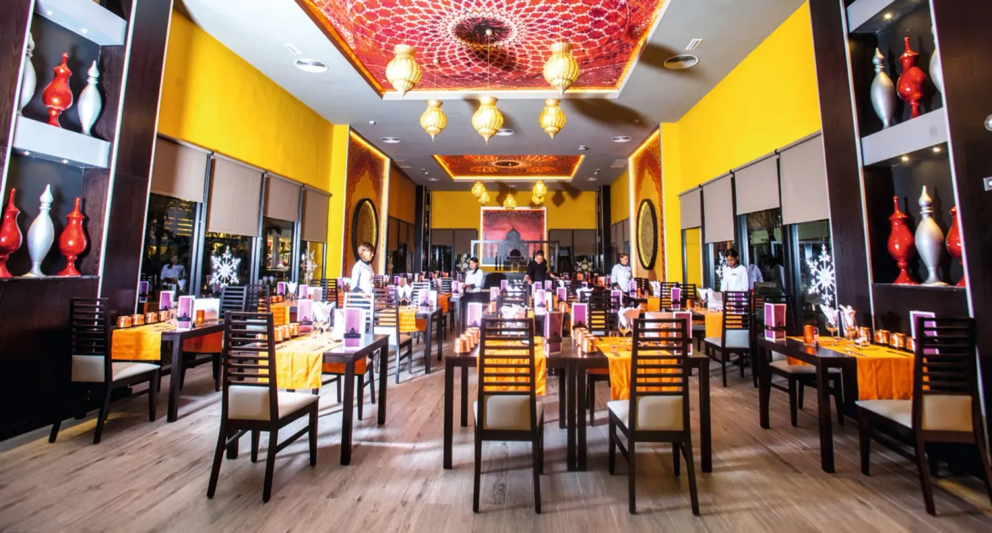 Bright yellow restaurant with ornate ceiling lamps and set tables at Hotel Riu Republica.