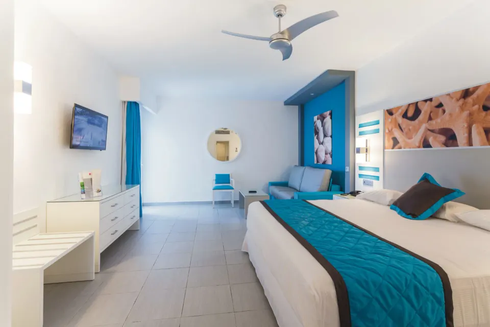 Bedroom with sofa, TV, dresser, and turquoise accents in the Room 2 Bedrooms at Hotel Riu Republica.