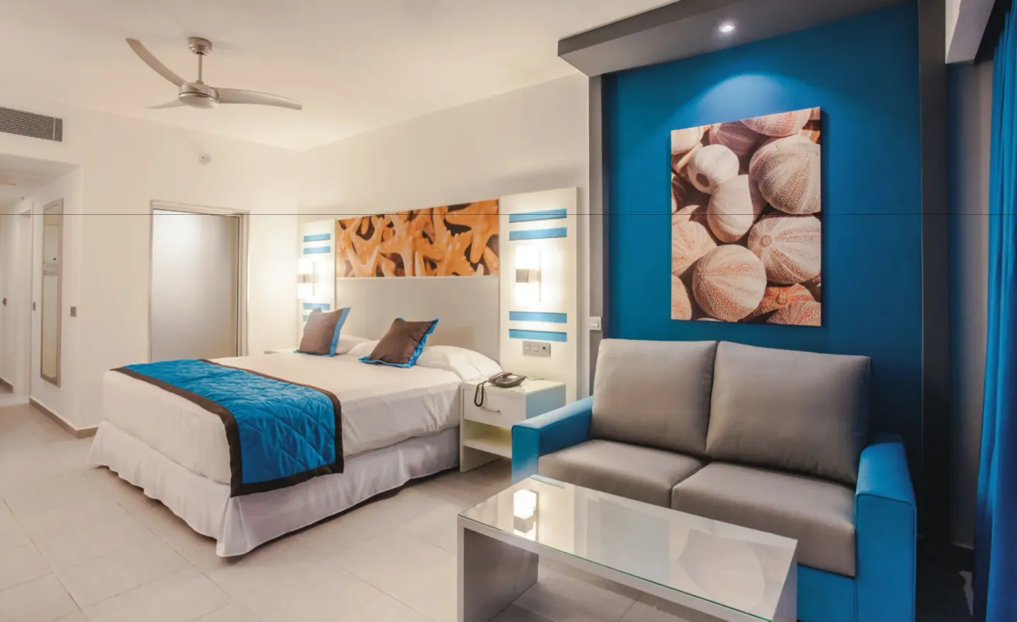 Guest room with king bed, sofa, glass table, and blue accent wall at Hotel Riu Republica.