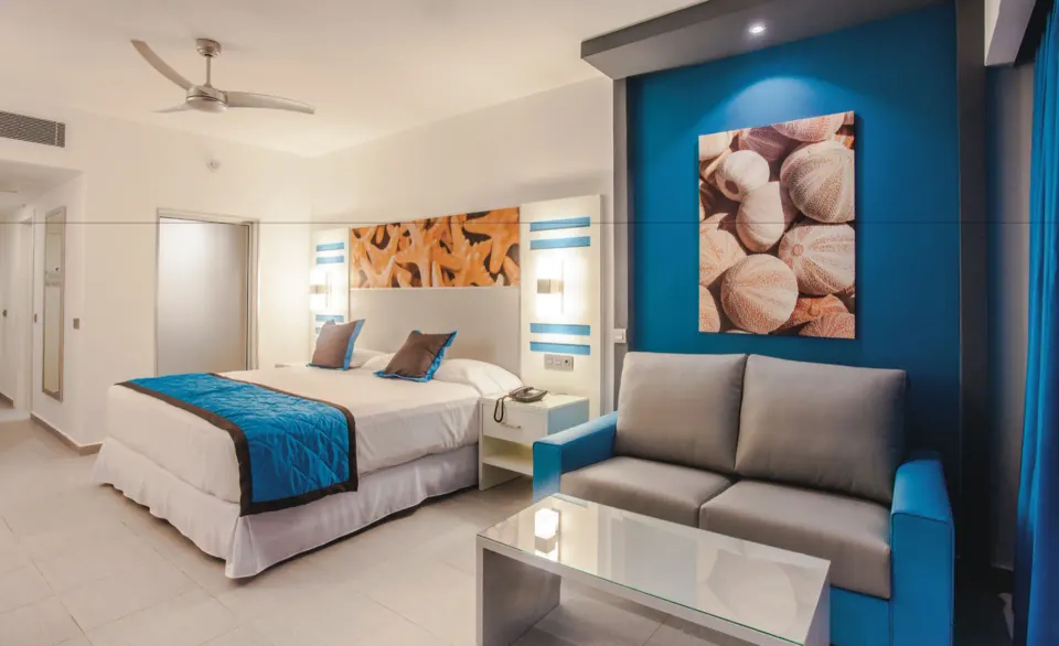 Guest room with king bed, sofa, glass table, and blue accent wall at Hotel Riu Republica.