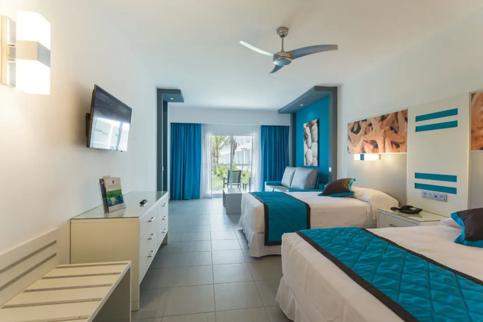 Guest room with two beds, sofa seating, TV, and balcony at Hotel Riu Republica.