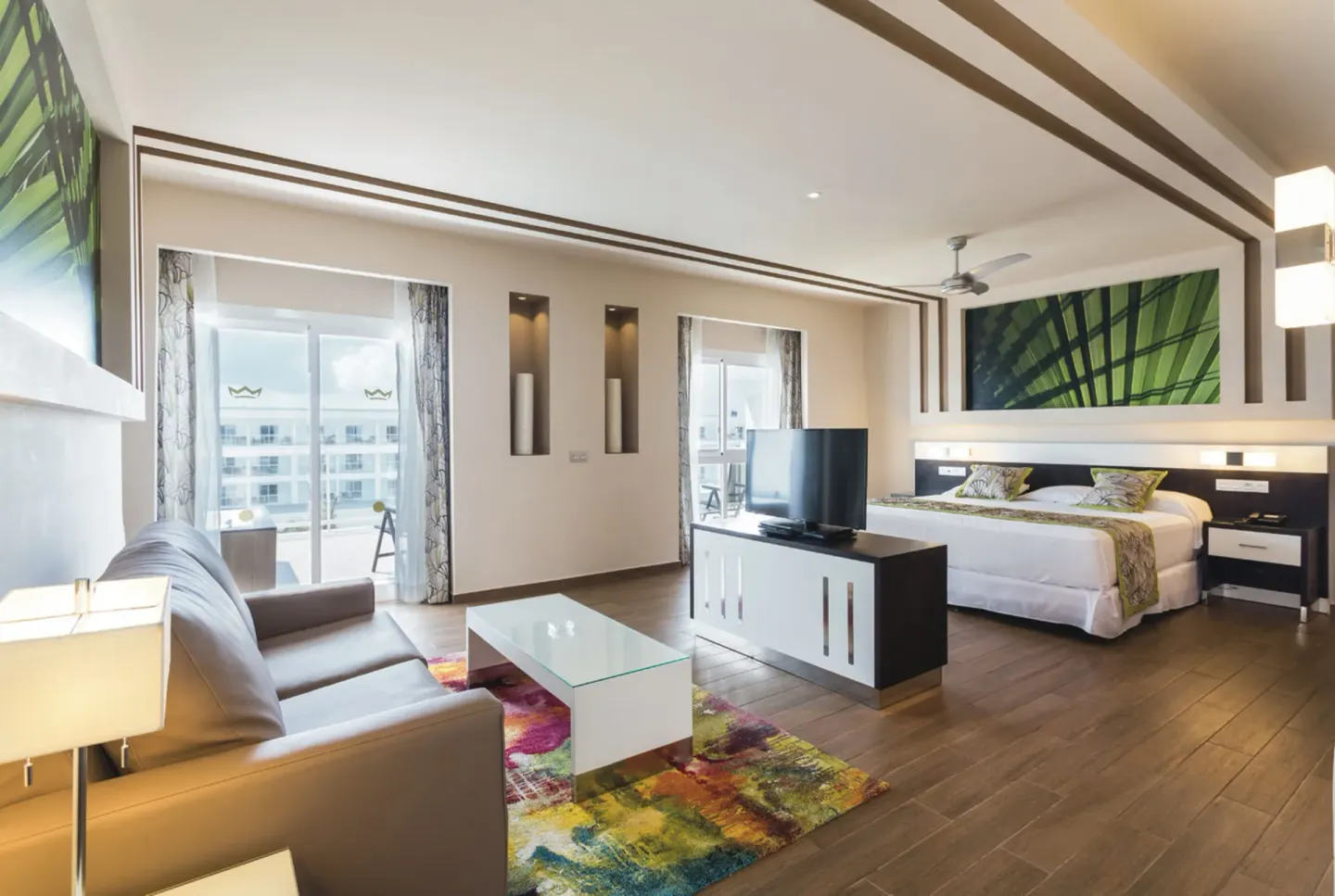 Suite with king bed, sofa seating, TV console, and balcony doors at Hotel Riu Republica.
