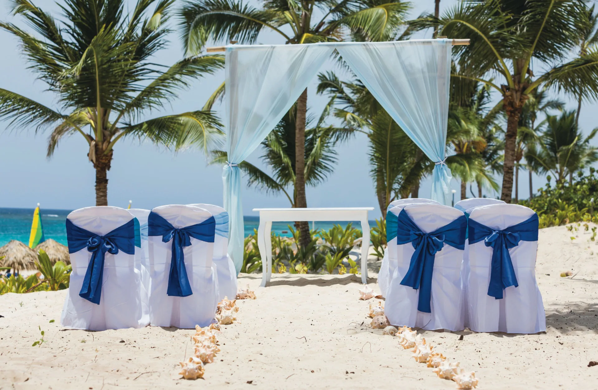 Beach wedding setup with white chairs and blue sashes at Hotel Riu Republica.