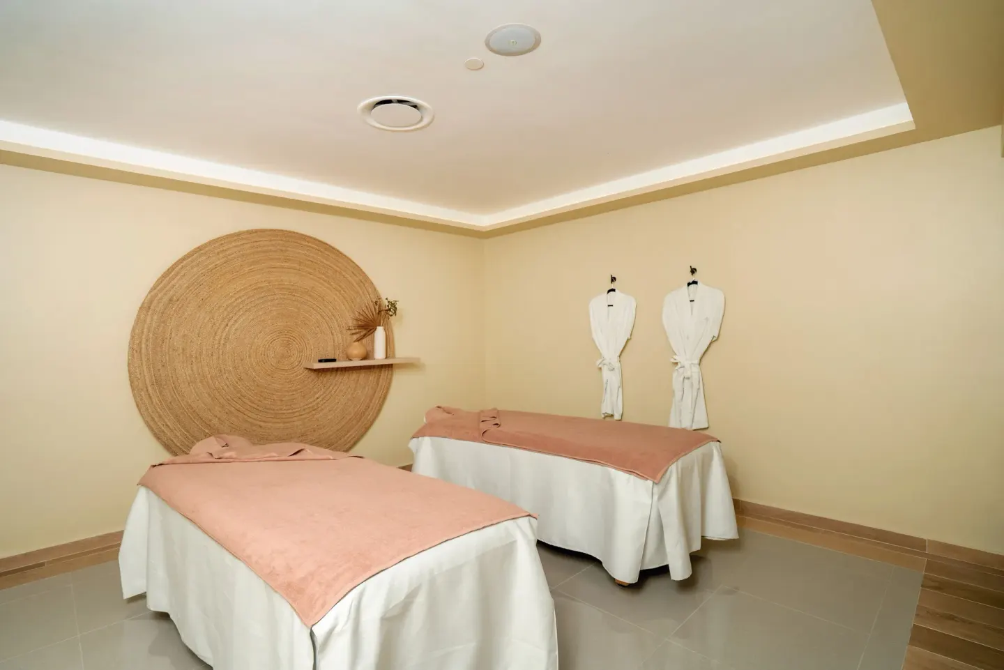 A spa room with two massage beds, robes, and woven wall decor at Hotel Riu Santa Fe.