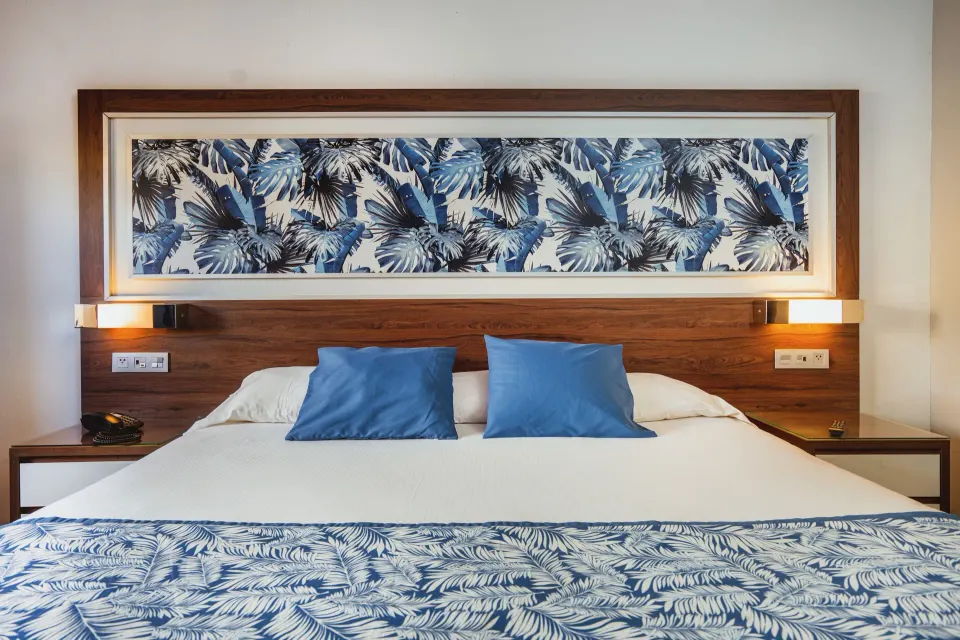 Hotel Riu Santa Fe bed at Hotel Riu Santa Fe with blue pillows and tropical wall art.