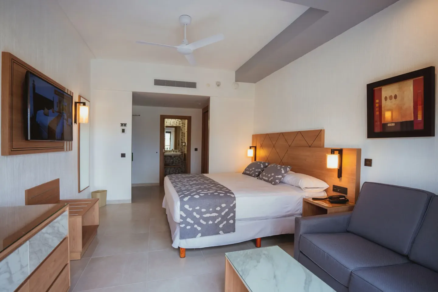Partial Ocean View guest room with bed, sofa and TV at Hotel Riu Santa Fe.