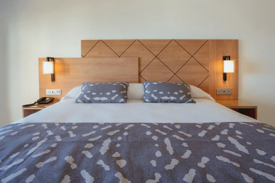 Suite Ocean View bed with wood headboard and wall lamps at Hotel Riu Santa Fe.