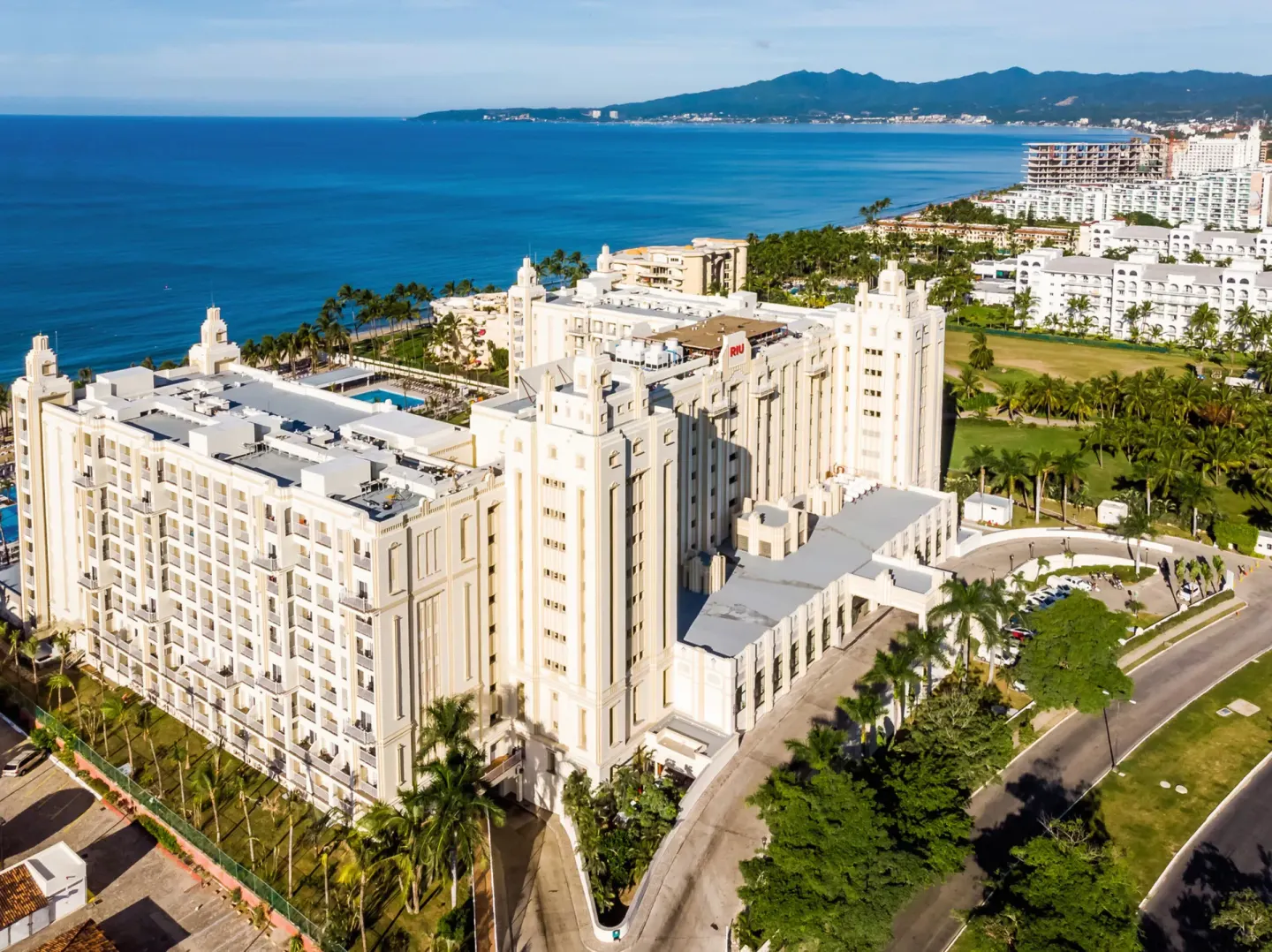 Aerial view of Hotel Riu Vallarta buildings with ocean and mountains nearby.