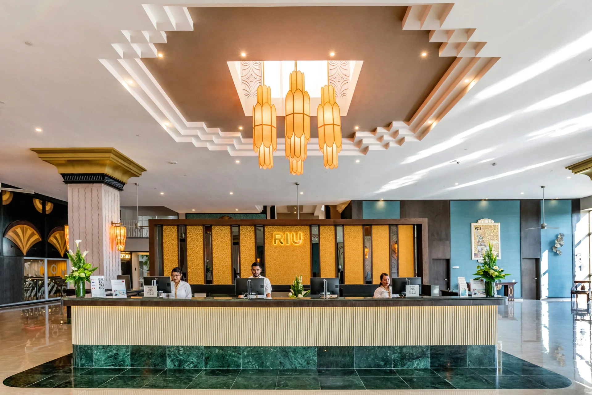 Front desk with staff and large pendant lights at Hotel Riu Vallarta.