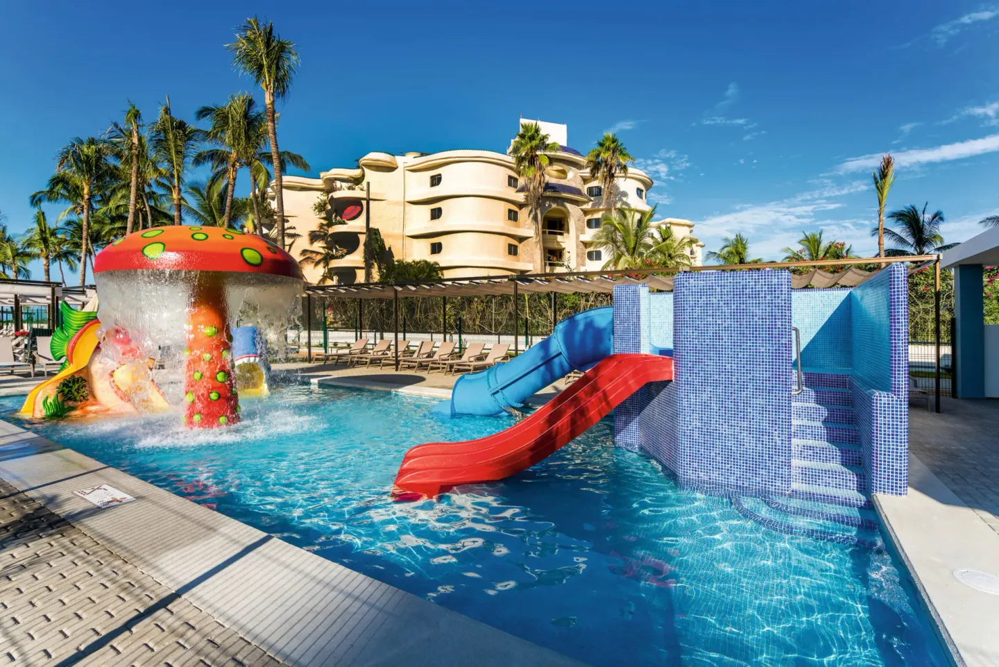 Kids' pool with red and blue slides and mushroom fountain at Hotel Riu Vallarta.