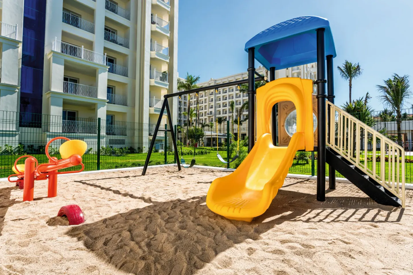 Playground slide and seesaw beside resort buildings at Hotel Riu Vallarta.