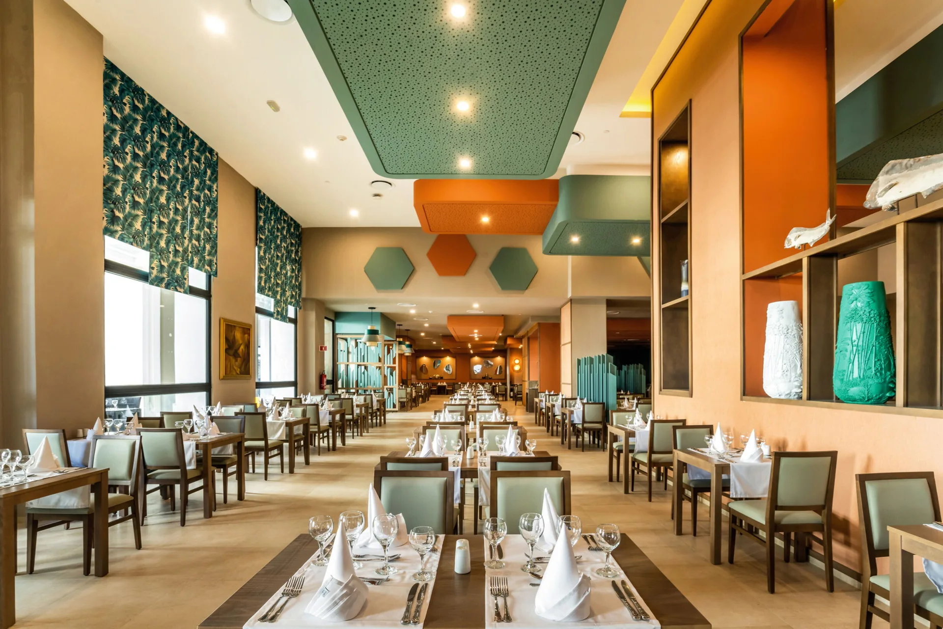 Long restaurant dining room with set tables and patterned wall panels at Hotel Riu Vallarta.