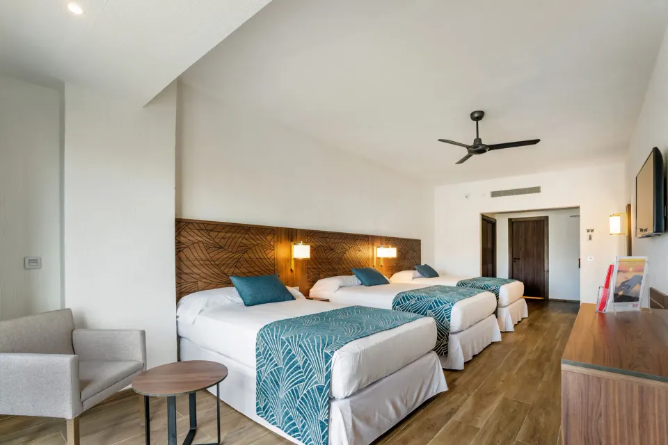 Family Room with three beds, armchair, dresser, and TV at Hotel Riu Vallarta.