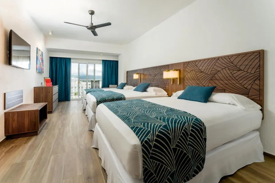 Family Room with three beds, teal accents, balcony doors, and TV at Hotel Riu Vallarta.
