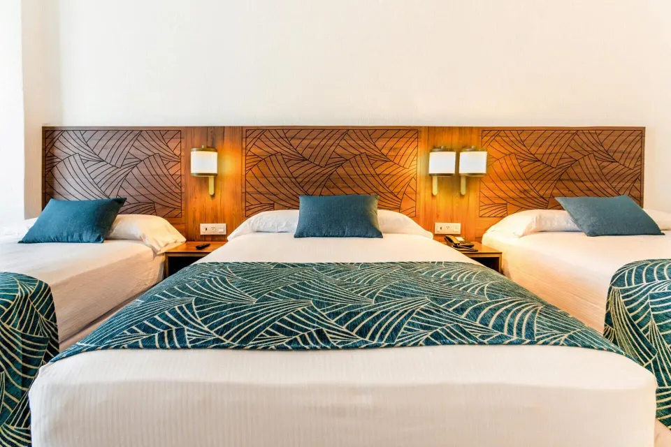Family Room beds with carved wood headboards and teal patterned covers at Hotel Riu Vallarta.