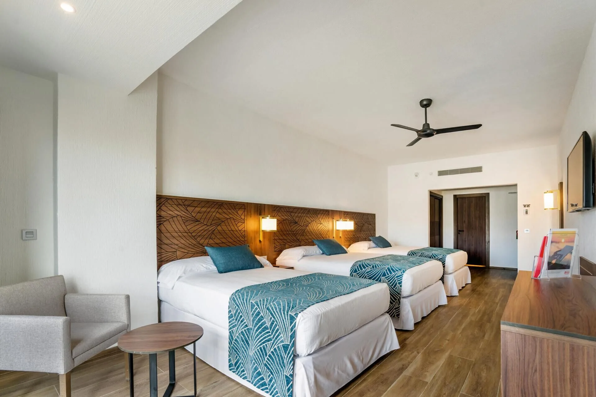 Family Room with three beds, seating area, dresser, and wall-mounted TV at Hotel Riu Vallarta.