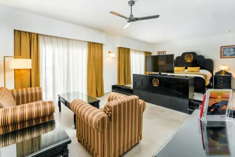 Ocean View Suite seating area with armchairs, tables, TV, and raised bed at Hotel Riu Vallarta.