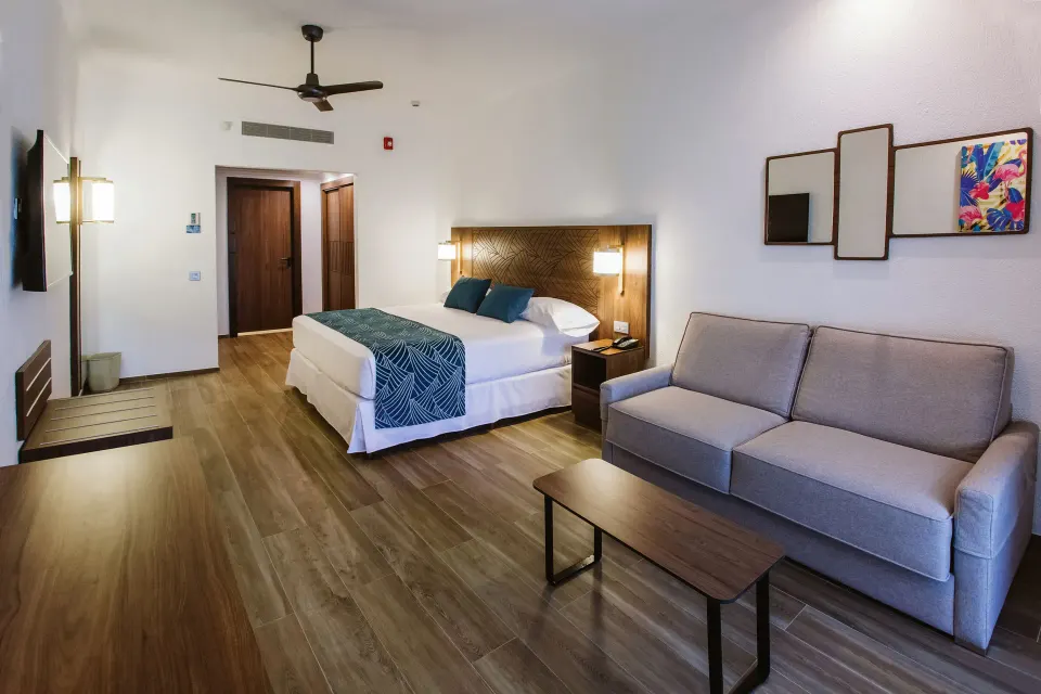 Partial Ocean View guest room with king bed and sofa at Hotel Riu Vallarta.