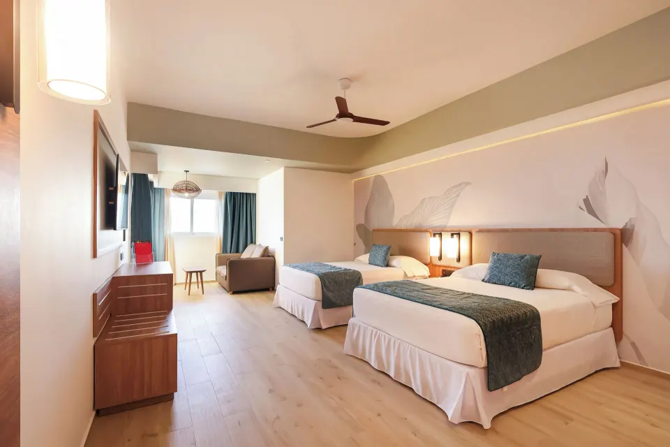 Family Room bedroom at Hotel Riu Ventura with two twin beds, TV console, sofa, and window seating area.