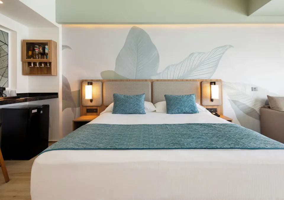 Oceanfront swim-up room king bed with leaf mural and refreshment nook at Hotel Riu Ventura.