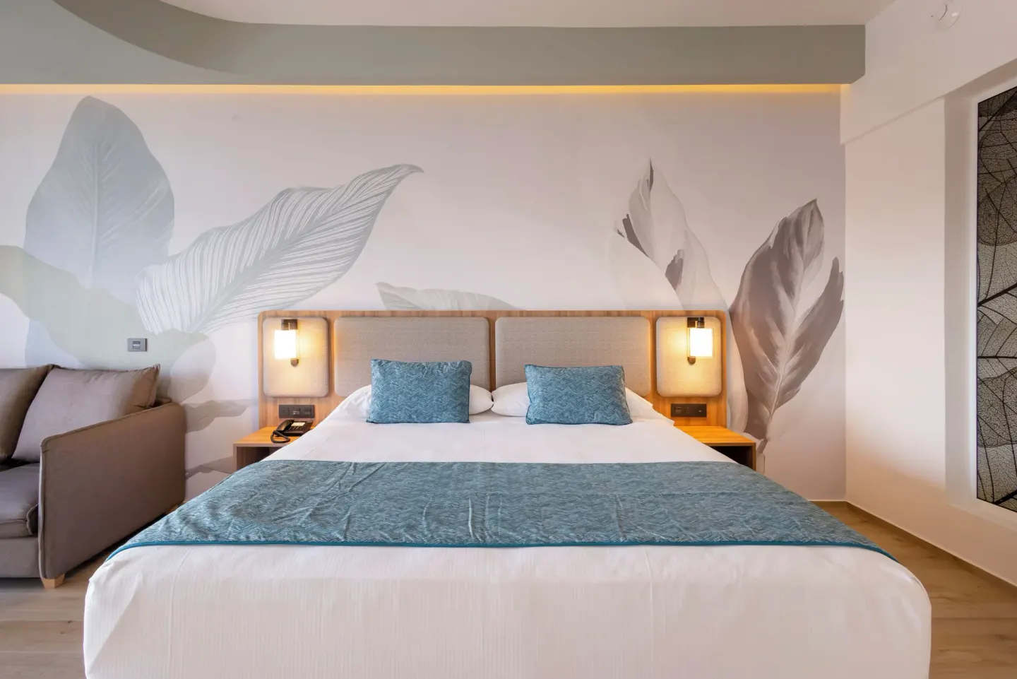 King bed with leaf mural and sofa in an oceanfront room at Hotel Riu Ventura.