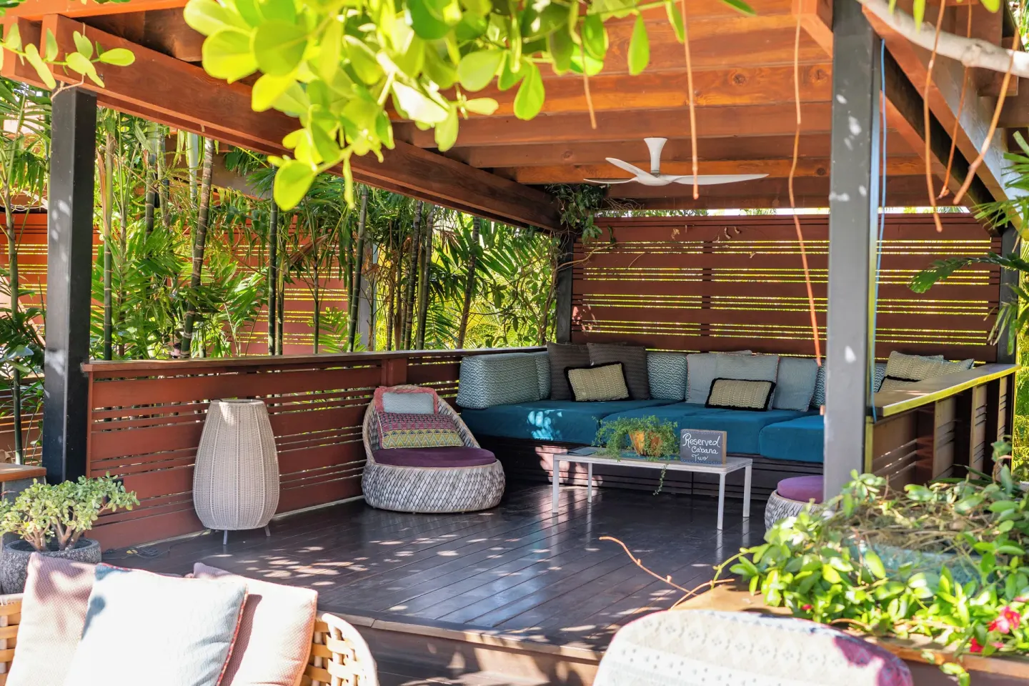 Covered pool cabana with sectional seating, pillows, and tropical plants at Hotel Wailea.