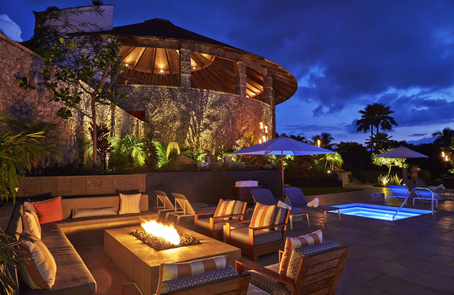 Evening fire pit seating beside the pool and illuminated stone building at Hotel Wailea.