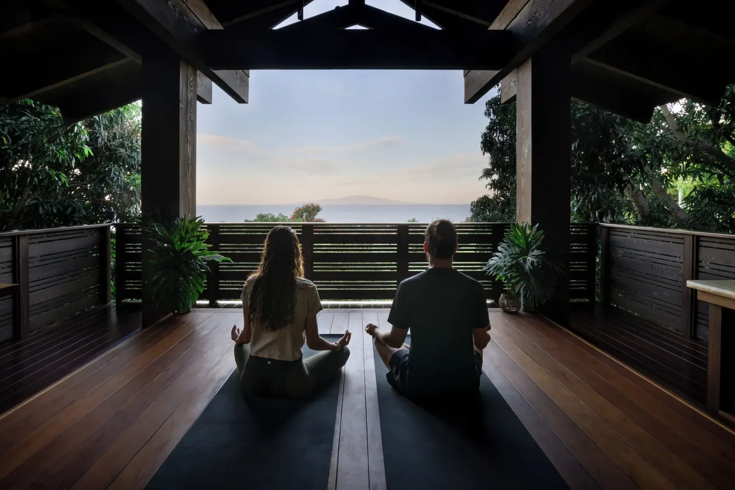 Two people seated in meditation on mats facing the ocean at Hotel Wailea.
