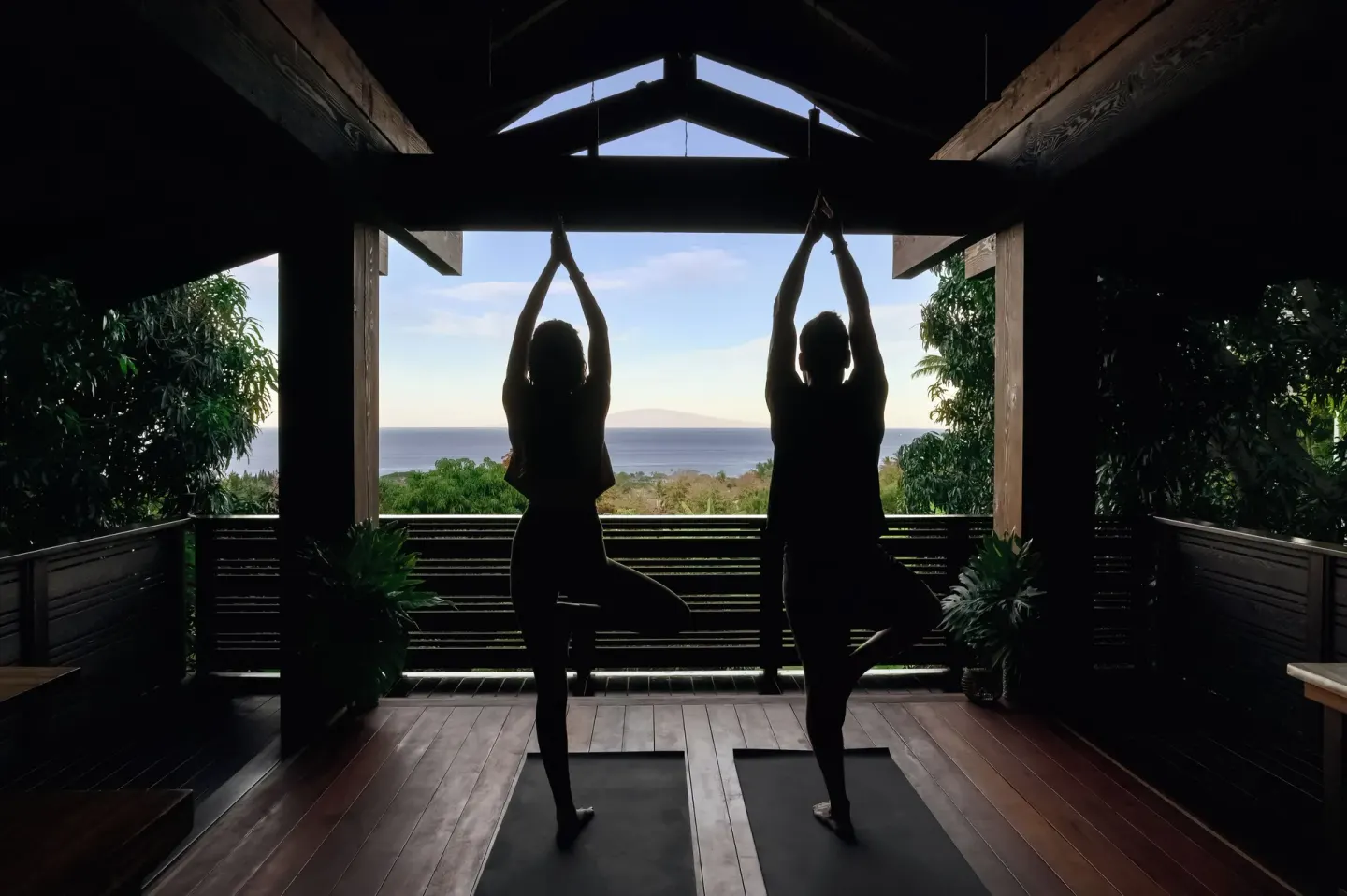 Two people practicing standing yoga poses in silhouette with ocean view at Hotel Wailea.