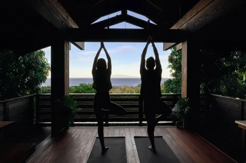 Two people practicing standing yoga poses in silhouette with ocean view at Hotel Wailea.
