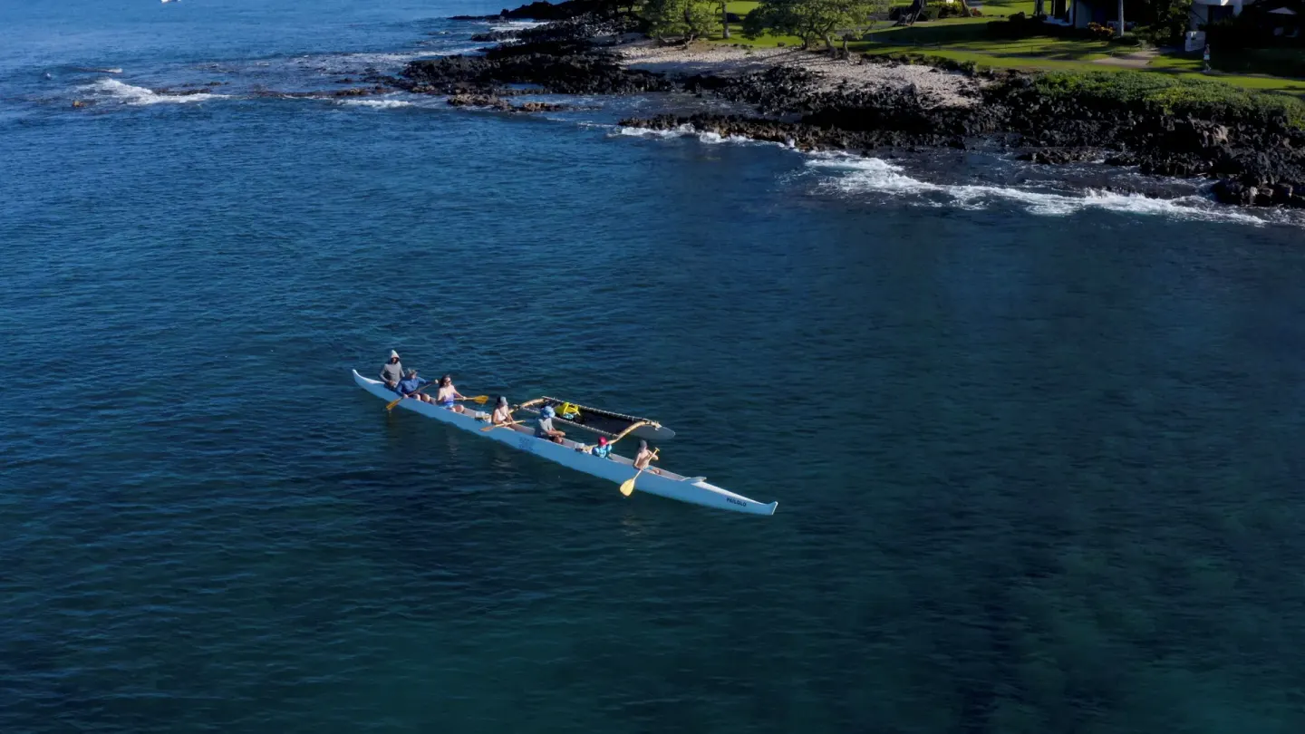 Paddlers in an outrigger canoe near a rocky coast by Hotel Wailea.