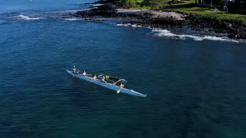 Paddlers in an outrigger canoe near a rocky coast by Hotel Wailea.