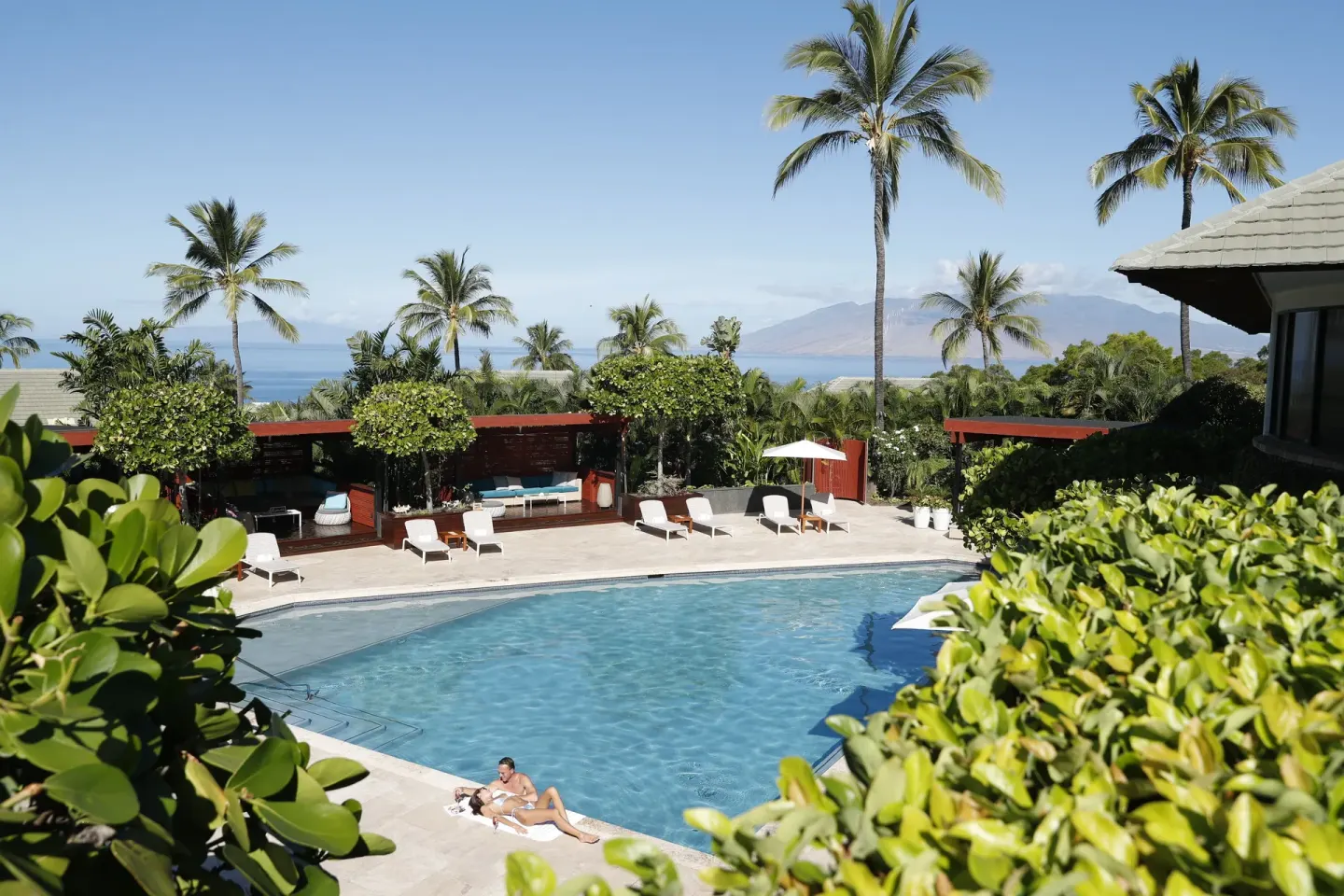Resort pool with palm trees, loungers, ocean, and island view at Hotel Wailea.