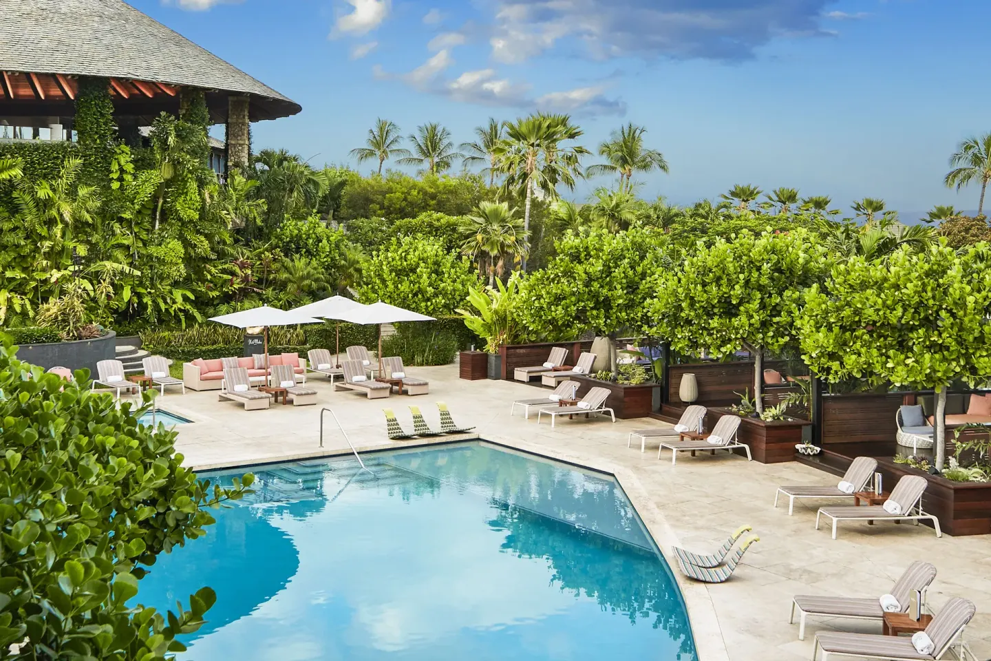 Resort pool with loungers, umbrellas, palms, and ocean beyond at Hotel Wailea.