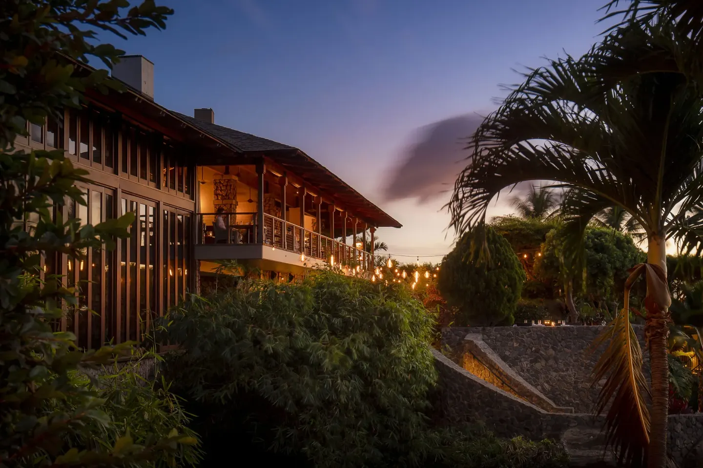 A lit restaurant building sits among palms and gardens at dusk at Hotel Wailea.