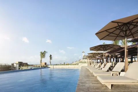 Infinity pool deck with rows of loungers and umbrellas at Hotel Xcaret Arte.